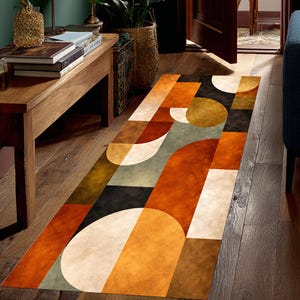 May include: A rectangular rug with a geometric pattern in shades of orange, brown, black, white, and olive green. The rug is placed on a wooden floor in a hallway. The design features various shapes.