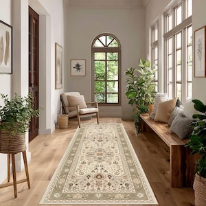 May include: A long, rectangular rug with an intricate floral pattern in cream, beige, and olive green tones. The rug is placed in a hallway with wooden floors, a wooden bench, and large windows. The room is decorated with plants and framed artwork.