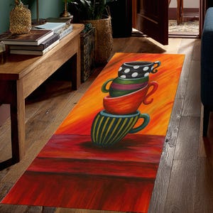 May include: A colorful, rectangular rug featuring a stack of teacups. The bottom cup has blue and yellow stripes, while the others are red, green, and polka-dotted. The background transitions from orange to red.