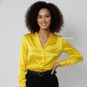 Puede incluir: Una mujer con una blusa de satén amarillo brillante con mangas largas y cuello en V. También lleva pantalones negros y un cinturón negro con hebilla plateada. La blusa tiene una textura brillante y suave. El texto "PremiumVastr" es visible.