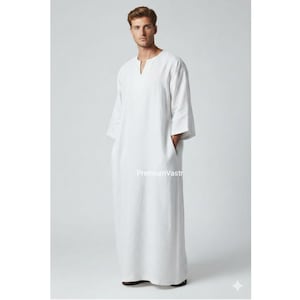 Può includere: Una veste bianca a maniche lunghe con scollo a V e tasche. La veste è realizzata in un tessuto leggero e ha una vestibilità rilassata. Il testo "PremiumVastr" è visibile sull'indumento.