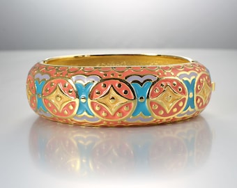 May include: A gold bangle bracelet with a colourful enamel design. The design features a repeating pattern of circles, stars, and swirls in shades of coral, turquoise, and lavender.