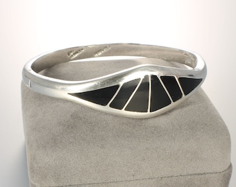 May include: A silver bangle bracelet with a black inlay design. The inlay is in the shape of a fan and is made of black onyx.
