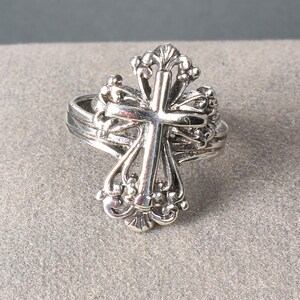 Peut inclure: Une bague argent&eacute;e orn&eacute;e d'une croix d&eacute;taill&eacute;e. La croix est orn&eacute;e d'&eacute;l&eacute;ments d&eacute;coratifs et d'une bande superpos&eacute;e. La bague est probablement en argent sterling ou en m&eacute;tal similaire, &eacute;voquant un th&egrave;me religieux ou symbolique.