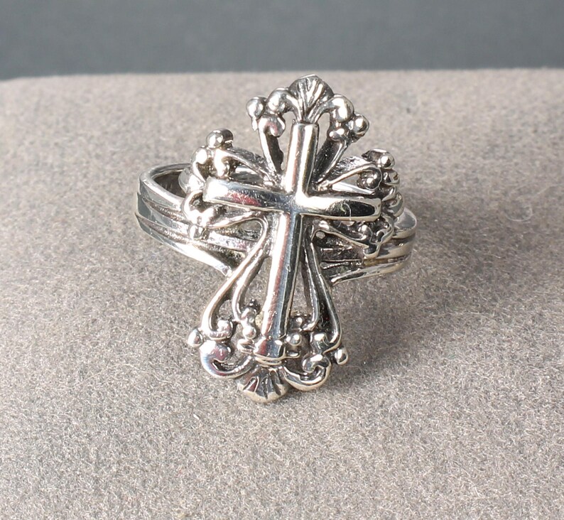 Peut inclure: Une bague argent&eacute;e orn&eacute;e d'une croix d&eacute;taill&eacute;e. La croix est orn&eacute;e d'&eacute;l&eacute;ments d&eacute;coratifs et d'une bande superpos&eacute;e. La bague est probablement en argent sterling ou en m&eacute;tal similaire, &eacute;voquant un th&egrave;me religieux ou symbolique.
