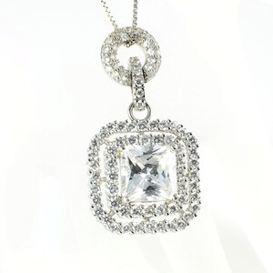 May include: A silver pendant necklace with a large square-shaped clear crystal surrounded by smaller crystals. The pendant is attached to a delicate silver chain with a circular design.