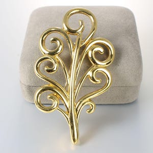 May include: A gold-toned brooch in the shape of a stylized leaf with intricate swirls and curls.