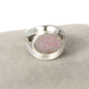 May include: A silver ring with a pink and white oval-shaped stone set in the center. The ring has a unique, curved design.