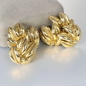May include: A pair of gold-toned leaf-shaped earrings. The earrings are made of metal and have a textured surface.