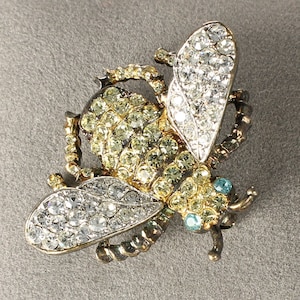 May include: A gold and silver bee brooch with clear and yellow rhinestones. The bee has a detailed body and wings.