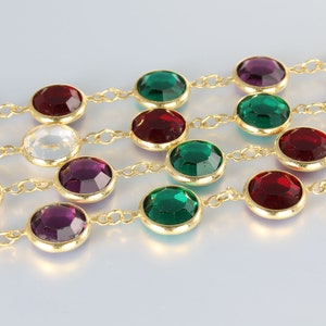 May include: A gold chain necklace with alternating clear, red, green, and purple faceted gemstones. The necklace is made of small, linked chains.