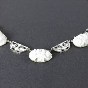 May include: A white cameo necklace with a silver chain and ornate silver accents. The cameos feature a floral design.
