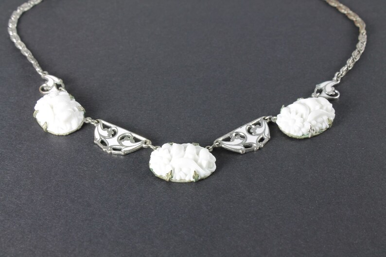 May include: A white cameo necklace with a silver chain and ornate silver accents. The cameos feature a floral design.