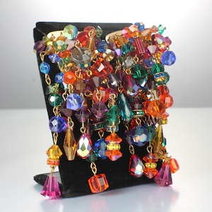 May include: A pair of large, colorful earrings with a cascade of beads in various shapes and sizes. The beads are in shades of red, orange, yellow, green, blue, purple, and pink.