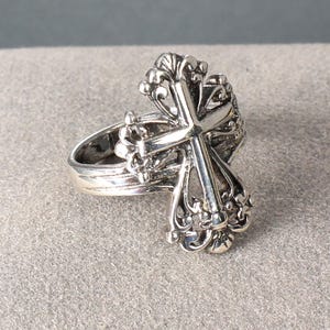 Peut inclure: Une bague argent&eacute;e orn&eacute;e d'une croix d&eacute;taill&eacute;e. La croix est orn&eacute;e de volutes et d'ornements complexes. Le corps de la bague est lisse, contrastant avec la croix &eacute;labor&eacute;e. La bague est probablement en argent sterling. Un bijou d&eacute;coratif.