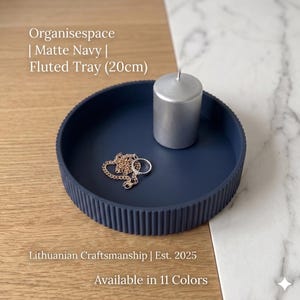 Op de afbeelding: Een marineblauwe, gegroefde tray van 20 cm diameter met een zilveren kaars, een gouden ketting en een ring. De tray staat op een houten oppervlak. De tekst op de afbeelding luidt "Organisespace | Matte Navy | Fluted Tray (20cm)".