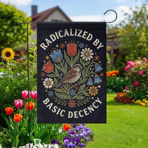 May include: Black garden flag with the text "RADICALIZED BY BASIC DECENCY" in white. The flag features a detailed illustration of a bird perched on a branch surrounded by colorful flowers, including tulips and daisies. The flag is displayed in a garden setting.