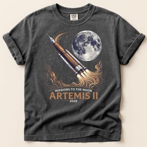 May include: A white ceramic mug with a black handle and the text "But First, Coffee" in a bold, black font. The mug is filled with a dark liquid, likely coffee, and sits on a light-colored surface.