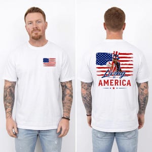 May include: A white short-sleeve t-shirt featuring a small American flag graphic on the front left chest. The back displays a large graphic of Uncle Sam over an American flag background with the text Living in AMERICA in red and blue lettering.