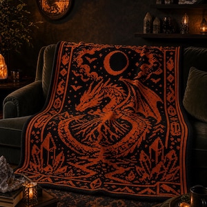 May include: A rectangular woven blanket featuring a black and orange color scheme. The design displays a central dragon motif surrounded by geometric patterns, crystals, and a crescent moon. The border consists of repeating linear and diamond shapes.