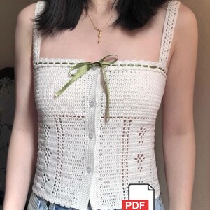 May include: A white crochet top with a square neckline and button-up front. The top features a green ribbon bow and decorative stitching along the neckline. The design includes floral and geometric patterns. A PDF icon is visible in the bottom right corner.