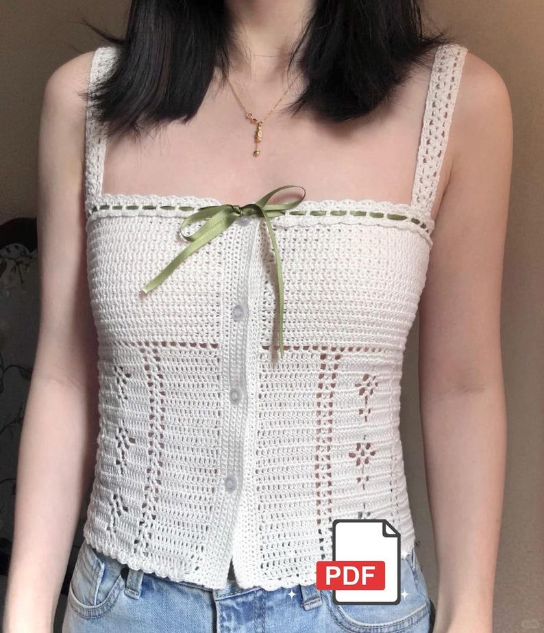 May include: A white crochet top with a square neckline and button-up front. The top features a green ribbon bow and decorative stitching along the neckline. The design includes floral and geometric patterns. A PDF icon is visible in the bottom right corner.