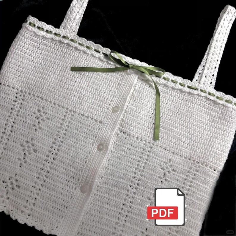 May include: A handmade white crochet top with a delicate openwork design. The top features a button-up front, shoulder straps, and a green ribbon bow. The edges are trimmed with a green stitch detail. A PDF icon is in the bottom right corner.