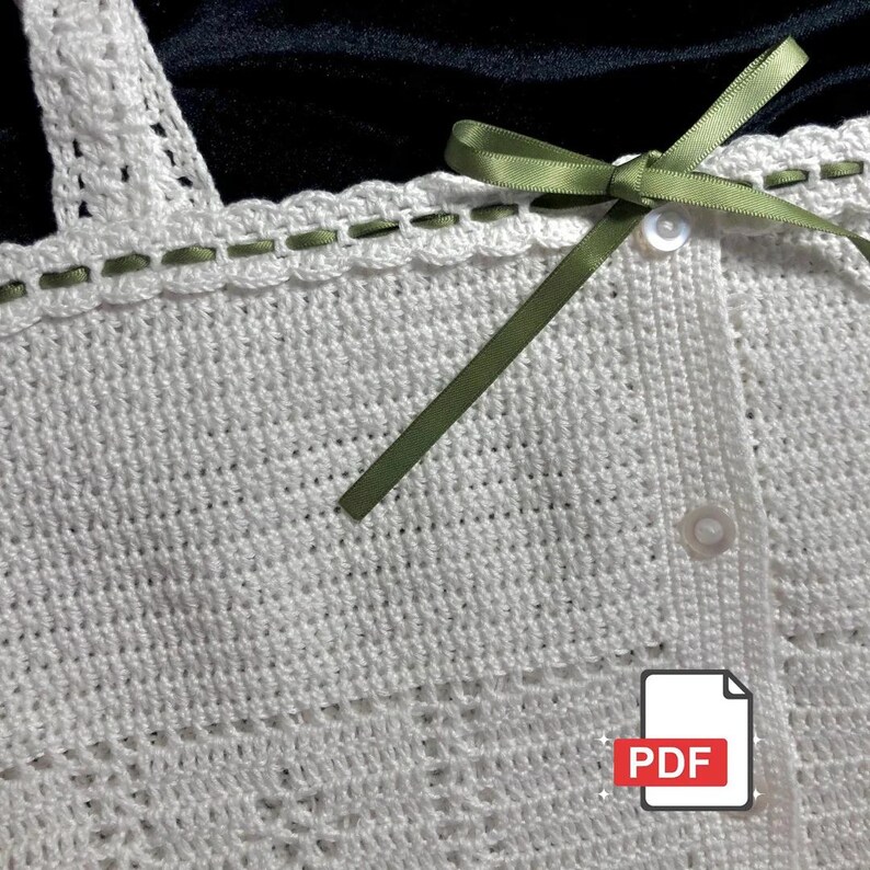 May include: Close-up of a white crochet top with a scalloped neckline and straps. The top features a delicate green ribbon detail along the neckline and a small bow. The top has a button closure. A PDF icon is in the bottom right corner.