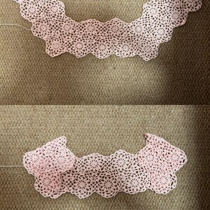 May include: Two handmade, light pink crochet collars. The collars are made of delicate, floral-patterned lace. The collars are displayed on a brown surface.