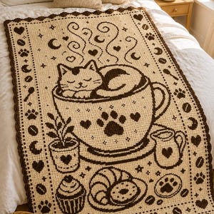 May include: A rectangular crochet blanket featuring a cream-colored base with dark brown patterns. The design displays a cat resting inside a large coffee cup, surrounded by motifs of a cupcake, a croissant, a small pitcher, and paw prints.