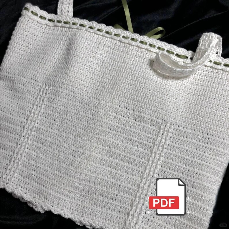 May include: A white, crocheted top with a scalloped edge and straps. The top has a textured pattern and is trimmed with a thin green thread. A PDF icon is in the lower right corner.