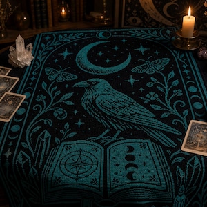 May include: A black and teal rectangular fabric cloth featuring a central raven perched on an open book, surrounded by crescent moons, moths, stars, and floral motifs. The design includes geometric patterns and celestial symbols in a woven texture.