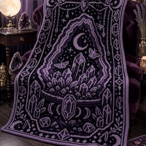 May include: A rectangular crochet blanket featuring a dark purple and black color palette. The design displays a central cluster of crystals, a crescent moon, and moths, all framed by geometric borders and smaller crystal motifs throughout.