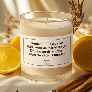 May include: A clear glass candle with white wax and a central wick, featuring a white label with black text that reads: Denke nicht nur an das, was du nicht hast. Denke auch an das, was du nicht kannst! The candle is surrounded by lemon slices, cinnamon sticks, and star anise.