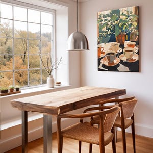 May include: A dining room scene featuring a natural wood table with metal legs and two woven-back chairs. A painting of coffee cups and plants hangs on the wall. A large window offers a view of fall foliage. A silver pendant light hangs above the table.