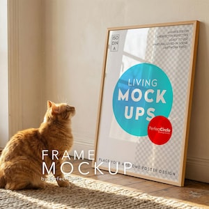 May include: A framed poster mockup with the text "LIVING MOCK UPS" in a room setting. A ginger cat sits on a rug, looking up at the poster. The frame is light wood, and the poster has a blue and red circle design.
