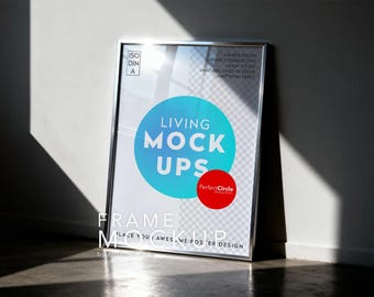 May include: A silver framed poster mockup leaning against a wall. The poster features the text "LIVING MOCK UPS" in a blue circle, with a red circle below it. The words "FRAME MOCKUP" are at the bottom.