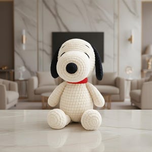 May include: A plush, off-white Snoopy doll with black ears and a black nose, wearing a red collar. The stuffed animal is sitting on a white surface. The background is a blurred living room.