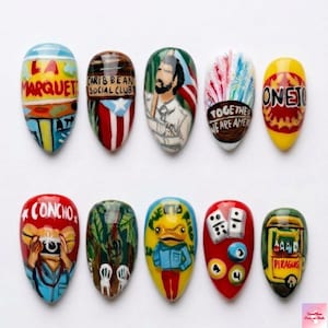 May include: A set of ten painted fingernails with various designs. The designs include text that reads "LA MARQUET", "CARIBBEAN SOCIAL CLUB", "TOGETHER WE ARE AMEN", and "CONCHO". Other designs include a frog, a bus, and a man.