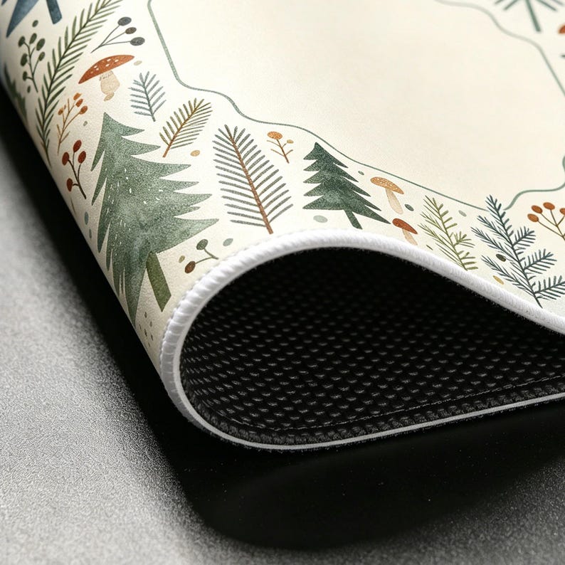 May include: A rolled-up, off-white mat with a forest-themed border. The border features watercolor illustrations of evergreen trees, mushrooms, and various foliage in shades of green, brown, and orange. The mat has a white stitched edge and a black, textured underside.