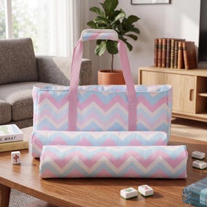 May include: A rectangular carrying bag and two matching cylindrical cases featuring a repeating chevron pattern in light blue, soft pink, and white. The bag has two pink fabric handles with a padded grip and a top zipper closure for storage.