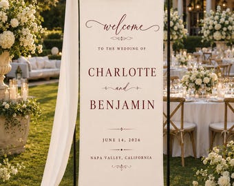 May include: A tall, rectangular off-white fabric wedding welcome sign suspended from a black metal frame, draped with white sheer fabric. The sign features dark red text: welcome to the wedding of CHARLOTTE and BENJAMIN, JUNE 14, 2026, NAPA VALLEY, CALIFORNIA.
