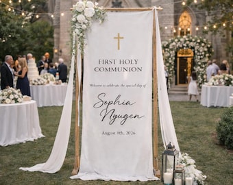 May include: A vertical white fabric banner suspended on a wooden frame, featuring a gold cross, the text FIRST HOLY COMMUNION, Welcome to celebrate the special day of, the name Sophia Nyugen, and the date August 8th, 2026, with white floral accents.