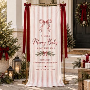 Könnte beinhalten: Ein vertikales Banner mit hellrosa und weißen Streifen, verziert mit einer roten Schleifenillustration, Tannenzweigen und dem Text A VERY Merry Baby IS ON THE WAY, HANNAH'S CHRISTMAS BABY SHOWER und DECEMBER 13, 2026, an einem goldfarbenen Metallständer.