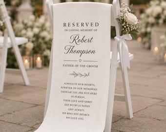 May include: A white chair with a cream-colored fabric draped over the back. The fabric is printed with the words "RESERVED" and "IN LOVING MEMORY OF Robert Thompson, FATHER OF THE GROOM." A floral arrangement with white roses and greenery is tied to the chair.