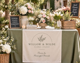 May include: A table covered with a sage green cloth and a white runner featuring the text Willow & Wilde Floral Studio Flowers for Meaningful Moments. The table displays floral arrangements in vases, a candle, books, and wooden signs with text.