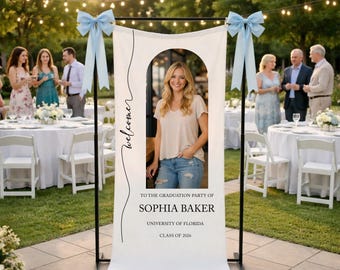 May include: A white graduation party banner with a photo of a woman, the word "welcome", and the text "To the Graduation Party of Sophia Baker, University of Florida, Class of 2026". The banner is decorated with light blue bows.