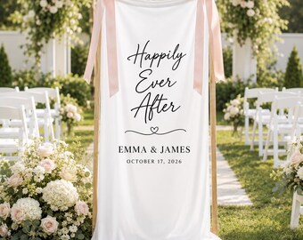 May include: A white fabric wedding sign hanging on a wooden frame with two light pink ribbons tied at the top corners. The sign features the black text "Happily Ever After" above the names "EMMA & JAMES" and the date "OCTOBER 17, 2026".