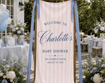 May include: A vertical fabric banner with light pink and white vertical stripes, featuring dark blue text that reads Welcome to Charlotte's Baby Shower, The Garden House, August 29, 2026. The banner is suspended from a wooden frame with blue ribbons.