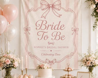 May include: A pink and white striped backdrop with the words "Bride To Be" in a decorative font. The backdrop is decorated with bows and a frame. The scene includes balloons, flowers, a cake, cupcakes, and candles, creating a festive atmosphere.